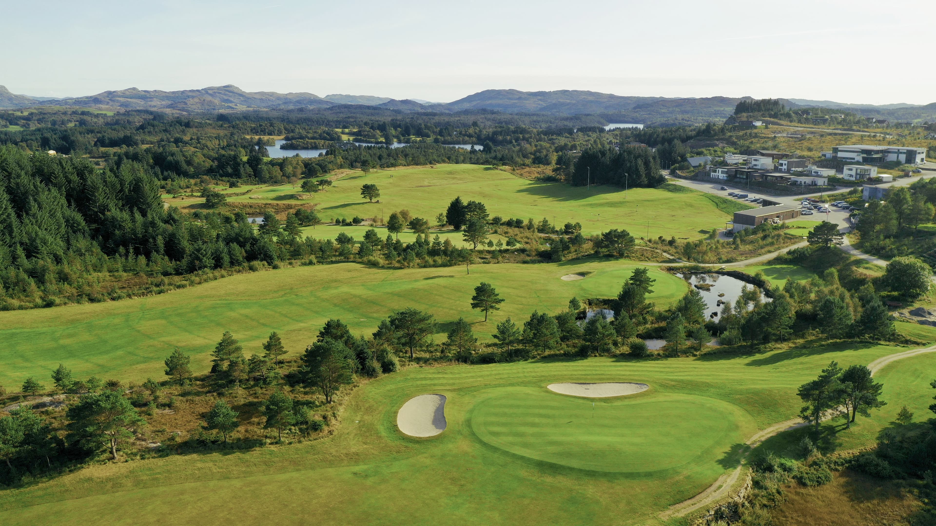 Oversiktsbilde over golfbanen med skog, vann og fjell i bakgrunnen